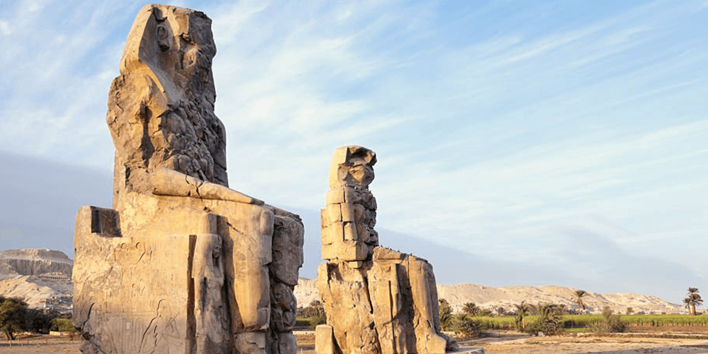 The two massive quartzite statues, the Colossi of Memnon, silhouetted against a golden-hour sky in Luxor, during an expert-guided private tour with Top Class Egypt Travel.