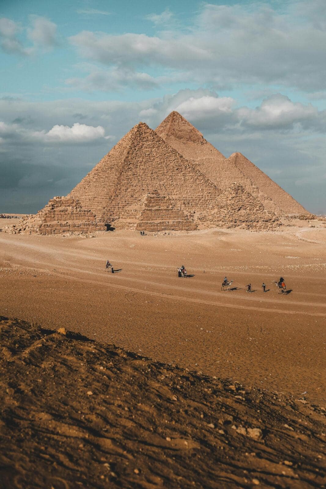 Side view of the Great Pyramids of Giza in the desert landscape, showcasing the massive scale of the limestone blocks under a clear sky.