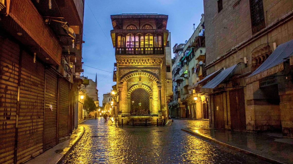 Illuminated historic Islamic architecture along the wet cobblestone path of Al-Muizz Street in Cairo at dusk