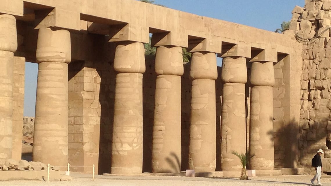 A close-up view of a row of massive, ancient stone columns with papyrus-shaped capitals at Karnak Temple in Luxor, showcasing the grand scale of ancient Egyptian architecture under a clear sky.