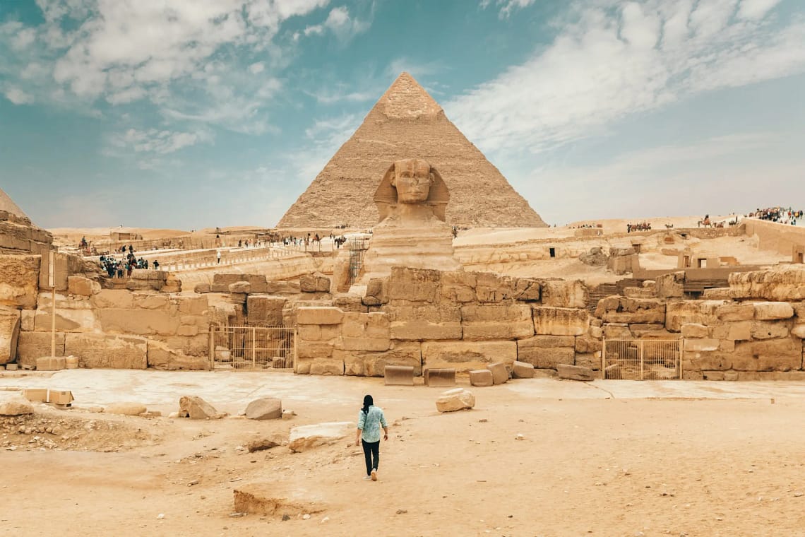 A person walking towards the Great Sphinx of Giza with the Pyramid of Khafre in the background