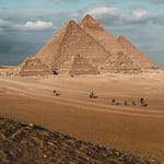 Side view of the Great Pyramids of Giza in the desert landscape, showcasing the massive scale of the limestone blocks under a clear sky.