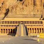 A straight daytime shot of the terraced Mortuary Temple of Hatshepsut at Deir el-Bahari in Luxor, showcasing its grand colonnades and long central ramp built into massive limestone cliffs.