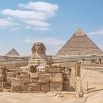 The Great Sphinx of Giza with the Great Pyramid of Khufu in the background under a clear blue sky, Cairo, Egypt.