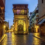Illuminated historic Islamic architecture along the wet cobblestone path of Al-Muizz Street in Cairo at dusk