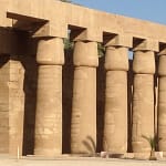 A close-up view of a row of massive, ancient stone columns with papyrus-shaped capitals at Karnak Temple in Luxor, showcasing the grand scale of ancient Egyptian architecture under a clear sky.