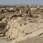 A high-angle view looking down at the massive Unfinished Obelisk carved directly into the pink granite bedrock of an ancient quarry in Aswan, under a clear sky. Caption A fascinating glimpse into ancient craftsmanship: the monumental Unfinished Obelisk