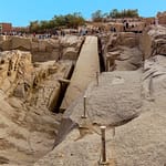 A high-angle view looking down at the massive Unfinished Obelisk carved directly into the pink granite bedrock of an ancient quarry in Aswan, under a clear sky. Caption A fascinating glimpse into ancient craftsmanship: the monumental Unfinished Obelisk