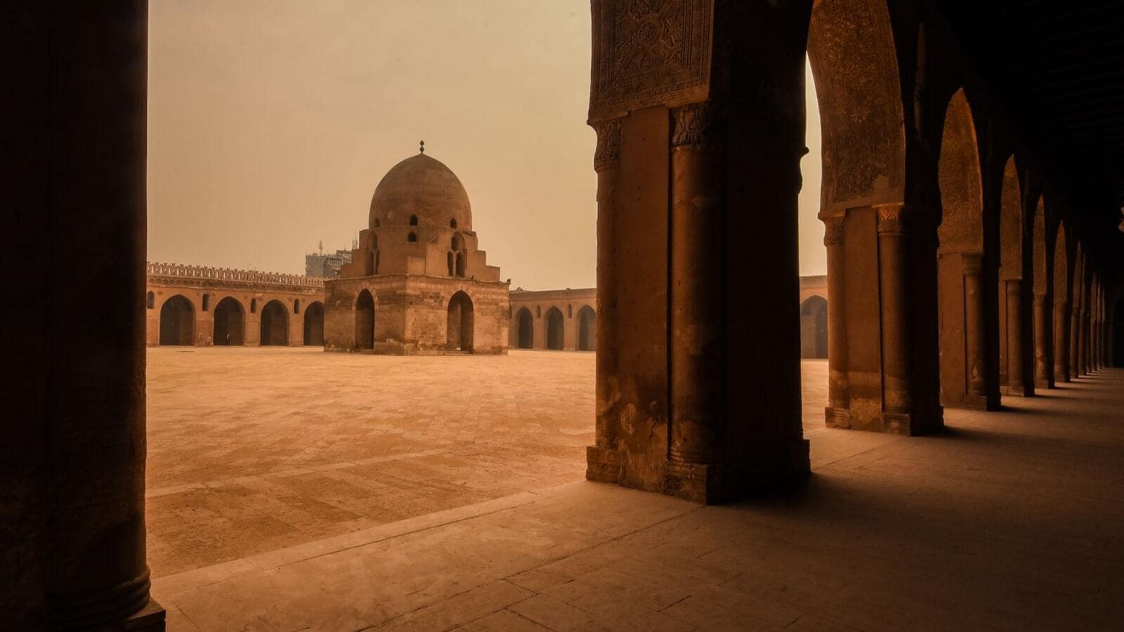 The open-air courtyard and architectural arches of the Mosque of Ibn Tulun in Cairo under a clear sky.