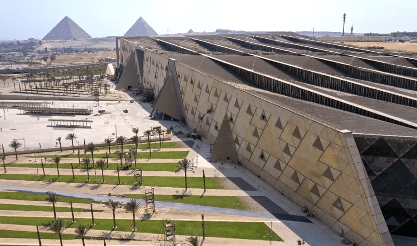 An aerial view of the modern Grand Egyptian Museum (GEM) complex with the Giza Pyramids in the background, a premier stop on private tours by Top Class Egypt Travel.